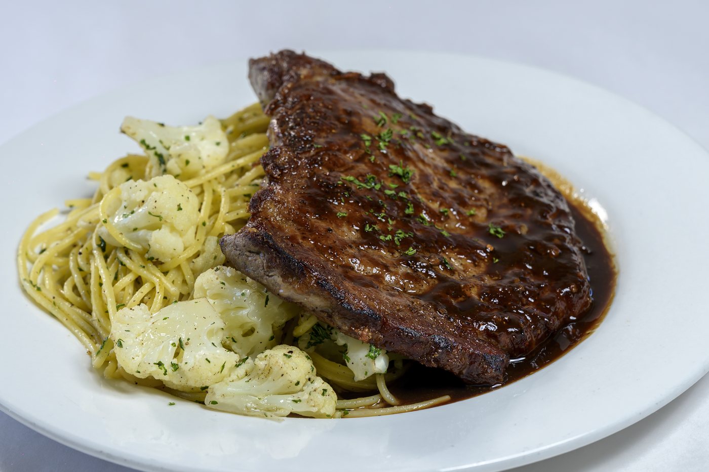 Grilled rib-eye steak with spaghetti, cauliflower and fresh thyme pan-jus